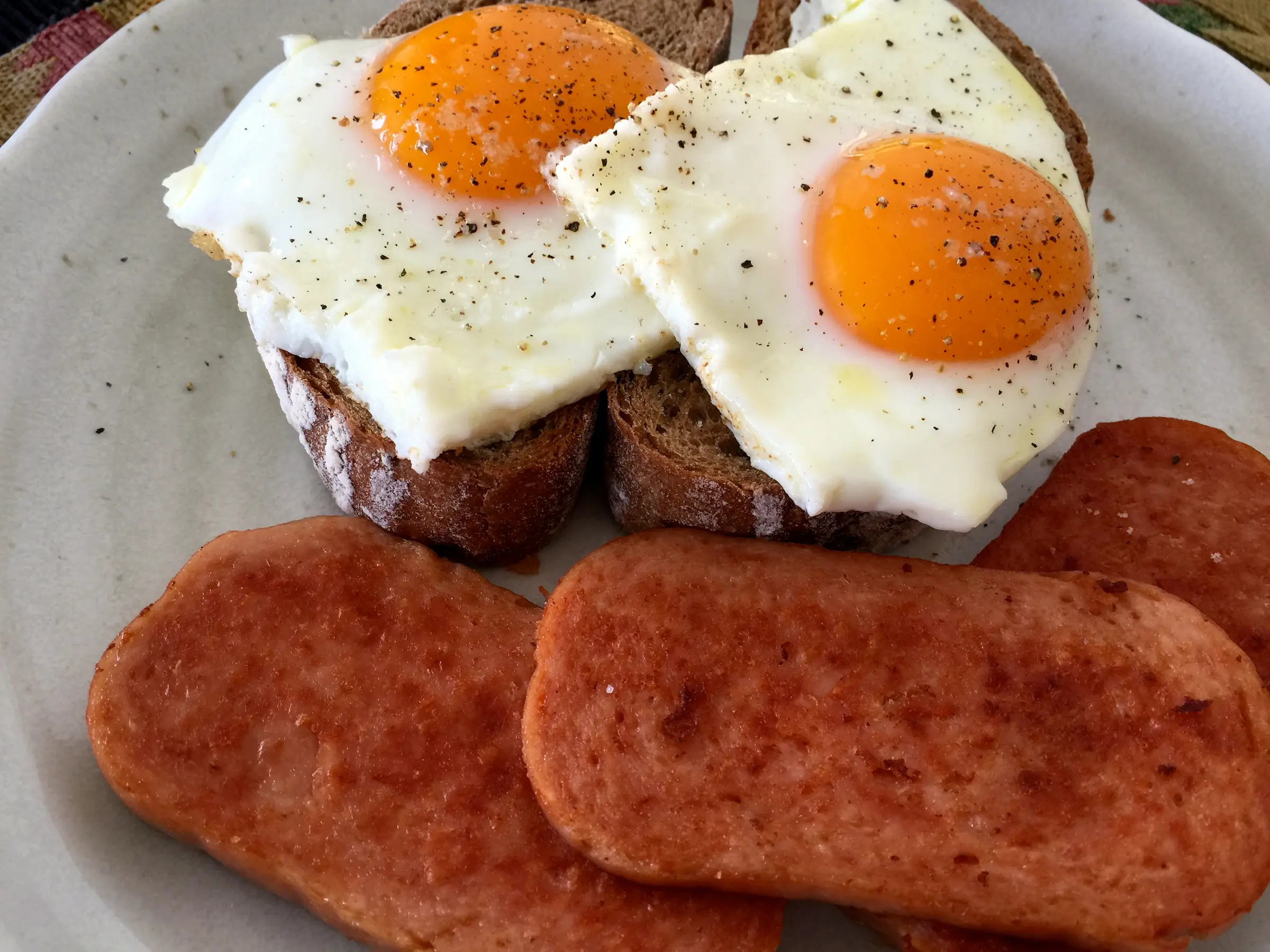 A zoomed in picture of a breakfast plate with two sunny side up eggs on toast next to three slices of cripsy spam
