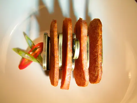 four pieces a fried spam in a silver tost holder on a plate. lettus and tomatoe garnish on the side